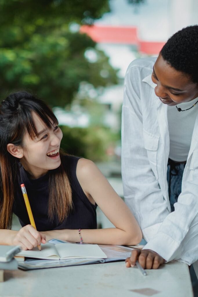 Happy young multiethnic ladies in casual outfit tutoring with books outside in summer day at table